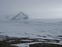 A pointy rock rises out of the snow and ice