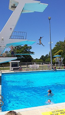 View of concrete diving tower next to a diving pool with children jumping off tower.