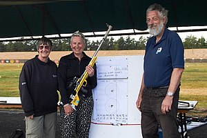 Three smiling people stand in front of a plotting sheet. The lady in the centre holds her Bleiker target rifle. She has just won the British Smallbore Rifle Championship for the second time.