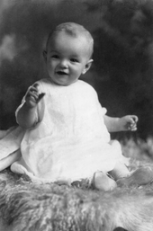 婴儿时的梦露，她穿着白色裙子，坐在羊皮地毯上