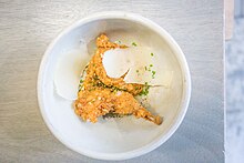 A couple of pieces of fried quail in a bowl, with onions and rosemary sprinkled on top of and around the quail pieces.