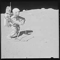 John Young using the rake tool to collect a sample (67700) at the southeast rim, with the rover at the central horizon, and white breccia boulders at the right horizon