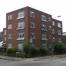 Three-quarter view of a four-storey red-brick block of flats on a corner site. One section projects, and two other parts are mostly hidden to the left and right. A sign reads "Florence Court".