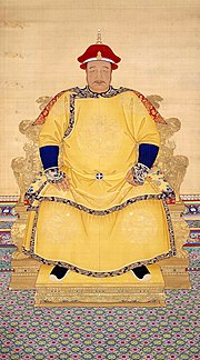 Full-face painted portrait of a corpulent man with a thin mustachio wearing a red hat and a multilayered yellow robe with dragon decorations, and sitting on a throne mounted on a low podium.