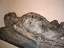 A sculpture of a dead body lying down, in an advanced stage of decay