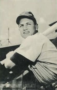 A man wearing a baseball cap and jersey poses prior to swinging his baseball bat.