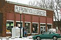 A photograph of a brick building with a painted wooden sign saying "Pleasantville Grocery"