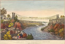 A man, two woman, and a dog are in the left foreground, viewing a bridge that spans a river. The bridge is suspended on lines that are supported by two stone towers on each side of the river and anchored by lines to each shore. The bridge has two levels; a train travels on the top level, while people and horse-drawn carriages cross on the bottom. In the river, downstream from the bridge, a boat is visible. In the distance is Niagara Falls.