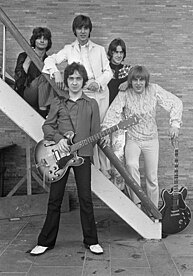 A rock band of five men posing on an outdoor stairwell.