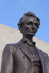 The upper portion of a large outdoor metal statue of Abraham Lincoln, beardless and thoughtful