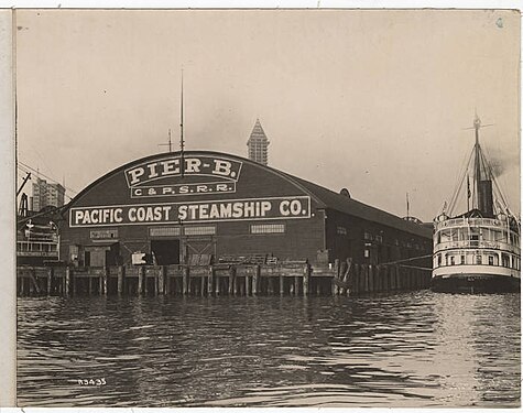 Pier B. Museum of History and Industry dates this 1913, and it certainly can't be any earlier because the Smith Tower has topped out in the background. At this date, the shed end of Pier B reads, "Pier B." "C. & P. S. R. R." (Columbia & Puget Sound Railroad), "Pacific Coast Steamship Co."