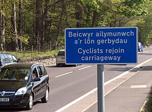 Blue road sign with white writing: "Beicwyr ailymunch a'r lôn gerbydau" / "Cyclists rejoin carriageway".