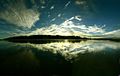 Panorama of Cox's Bazar in the early morning: clouds on a blue sky, still water and forest in the distance.