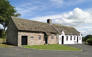 A long, one-storey rural building built of stone and divided into two halves; the right half, which is used as a chapel, is whitewashed.