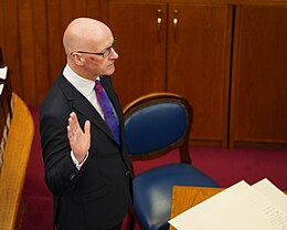 John Swinney raises his right hand over parchments in a courtroom