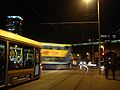 A Dublin Bus double-decker crosses tram tracks, as a Luas tram waits, and the DART crosses a bridge in the background.