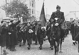 Soldiers, some carrying flowers, led by a soldier on horseback