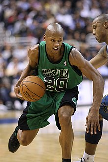 A basketball player dribbles around a defender