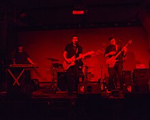 A rock band performing on stage with red lights