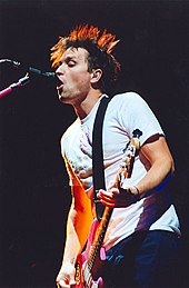 A man playing bass guitar sings into a microphone.
