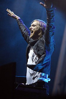 A light-skinned, long-haired man smiles and raises his arms.