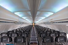 Cabin of the 757. There are six seats per row, with a single aisle separating the seats. Light shines through the side-wall windows and overhead lighting