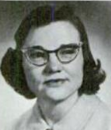 A young white woman with dark hair in a "flip" style, wearing cat-eye glasses and a collared blouse