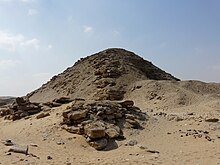 The rubble mound remains of a pyramid with large stones jutting out from beneath