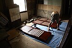 A man repainting the frames and muntins of three capiz-shell window sashes.