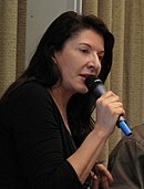 Marina Abramović looking to her left and speaking on a microphone.