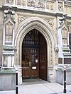 Surrounded by Gothic architecture and enclosed in a pointed arch is a pair of wooden doors, the entrance to the court.