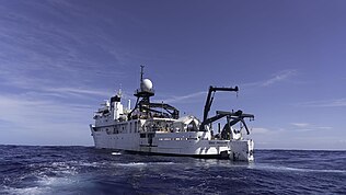 A large support vessel with a small rectangular profile deep submergence vehicle suspended over the water at the stern