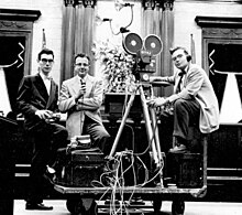 Three men standing with a WTVJ film camera