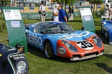 A light blue and red 1970s closed-cockit racing car on display out of doors in a car show