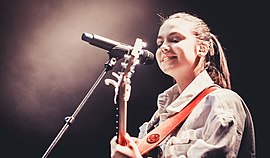 A teenage girl plays guitar on stage