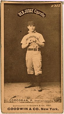 Baseball card with photo of full shot of man standing wearing a baseball uniform. The cap is dark and the shirt says "Indianapolis". Near the top of the photo are the words "Old Judge Cigarettes" and near the bottom are the words :CORCORAN, P, Indianapolis. At the bottom of the card beneath the photo it states "GOODWIN & CO. New York.