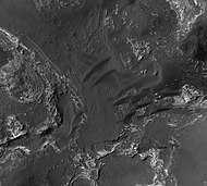 Orson Welles Crater, as seen by HiRISE. Layered, light-toned rocks seem to be under a dark mantling material. Layers may be sandstone, volcanic ash, or lakebed deposits.