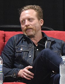 A man with ginger hair and a ginger beard looking to the left of the camera.