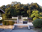 Torii gate behind a white stone fence in front of trees.