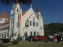 A large white church with a mass of people in front of it