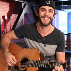 A bearded young man smiling broadly and playing a guitar