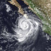 A photograph of a hurricane near the southern tip of the Baja California peninsula; it has a small eye, its convection has some tiny holes in it, and there are small breaks in the spiral banding