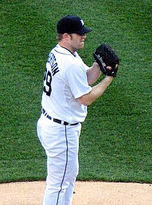 A man wearing a white baseball uniform and a dark baseball cap