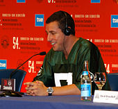 Adam Sandler with headphones on sitting at a desk.