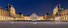 The Louvre pyramid, a gray structure, sits in the center of a courtyard, surrounded by ancient buildings.