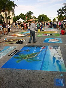 Street scene with multiple street paintings and a crowd of spectators in the distance.