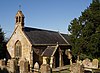 Stone building with arched window and slate roof. In the foreground are gravestones.