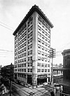 Ground-level view of a 10-story building with a rectangular cross section and a gray brick facade