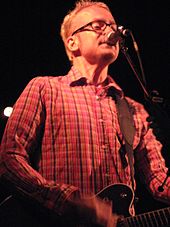 A color photograph of Chris Collingwood, who is playing a guitar and singing live into a microphone.
