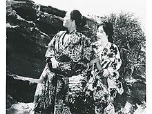 A still from Shima no onna (1920) with Henry Kotani and Yoshiko Kawada; two Japanese actors, a man and a woman, wearing printed kimonos, seated outdoors